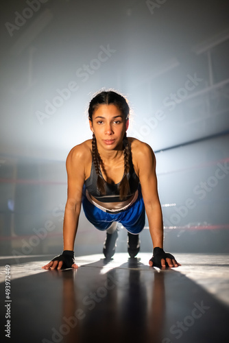Portrait of female boxer spending time in gym. Serious Caucasian girl in sportswear exercising in gym doing push-ups on hands on floor and looking at camera. Healthy lifestyle and women boxing concept © KAMPUS