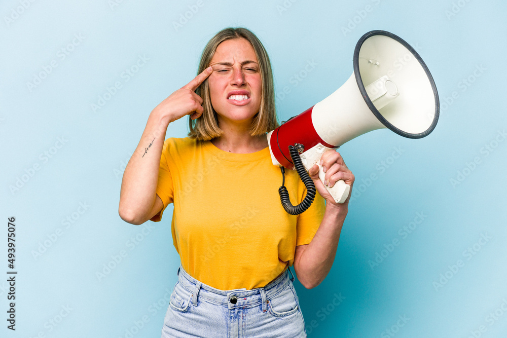 Young caucasian woman holding a megaphone isolated on blue background showing a disappointment gesture with forefinger.