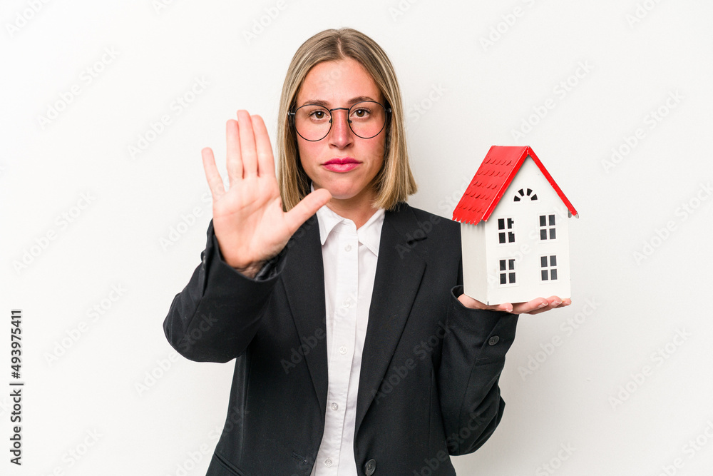 Young business caucasian woman holding a toy house isolated on white background standing with outstretched hand showing stop sign, preventing you. Young business caucasian woman holding a toy house isolated on white background standing with outstretched hand showing stop sign, preventing you.