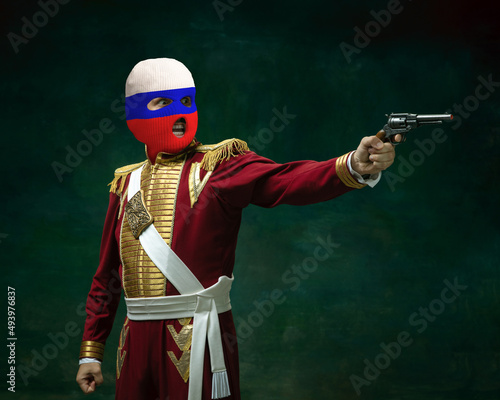 Portrait of man in suit as Nicholas II wearing red, white and blue balaclava isolated on dark green background. Retro style, comparison of eras concept. History photo