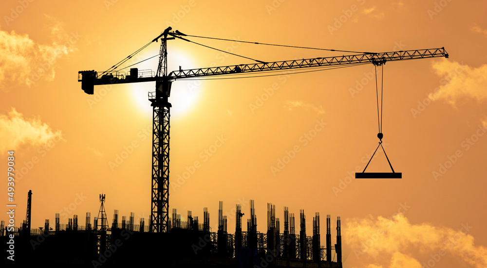 Silhouettes of tower construction cranes with yellow sky at morning time