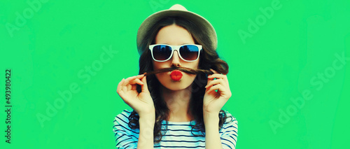 Portrait of funny young woman showing mustache her hair blowing lips with red lipstick sending air kiss on green background