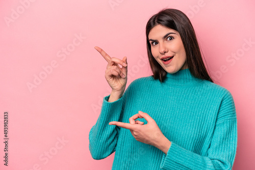 Young caucasian woman isolated on pink background pointing with forefingers to a copy space, expressing excitement and desire.