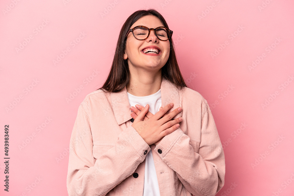 Young caucasian woman isolated on pink background laughing keeping hands on heart, concept of happiness.