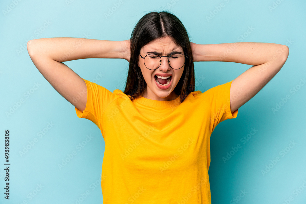 Young caucasian woman isolated on blue background covering ears with hands trying not to hear too loud sound. Young caucasian woman isolated on blue background covering ears with hands trying not to hear too loud sound.