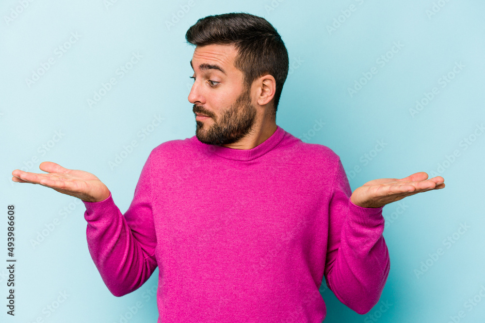 Young caucasian man isolated on blue background confused and doubtful shrugging shoulders to hold a copy space. Young caucasian man isolated on blue background confused and doubtful shrugging shoulders to hold a copy space.