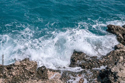 foamy waves of clear blue sea water beat against the rocky shore of the ocean
