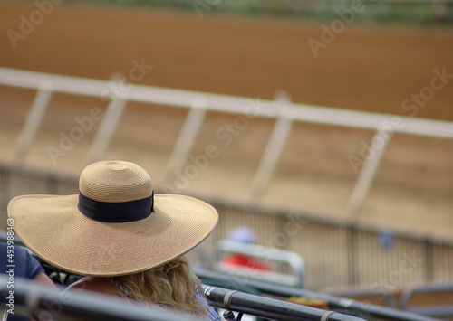 Foto View of a woman with a derby hat sitting hear the dirt track at a horse racetrack with depth of field background