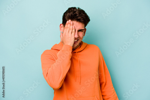 Young caucasian man isolated on blue background having fun covering half of face with palm.