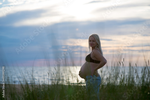 Beautiful Latvian pregnant woman standing at the beach during sunset