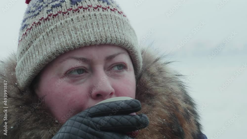 Slow motion portrait of a 45 year old woman drinking a hot drink from a cup under the snow. Cozy winter clothes for walking. Winter landscape Slow motion portrait of a 45 year old woman drinking a hot drink from a cup under the snow. Cozy winter clothes for walking. Winter landscape
