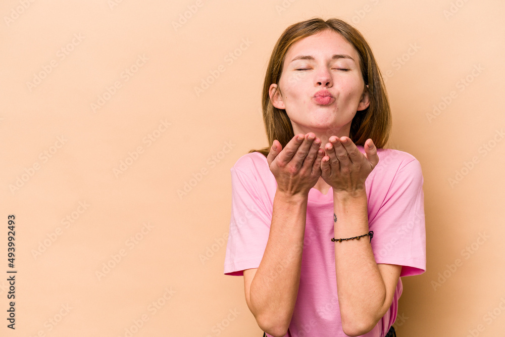 Young English woman isolated on beige background folding lips and holding palms to send air kiss.
