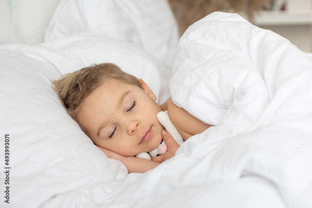 Beautiful blond toddler child, boy, sleeping in bed with teddy bear toy Beautiful blond toddler child, boy, sleeping in bed with teddy bear toy