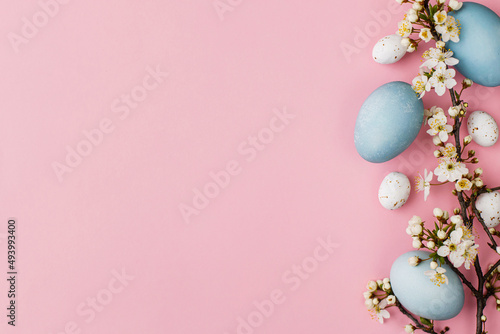 Stylish easter eggs and flowers flat lay on pink background. Modern natural dyed blue eggs and cherry blossom border. Greeting card template  easter background. Space for text. Happy Easter 