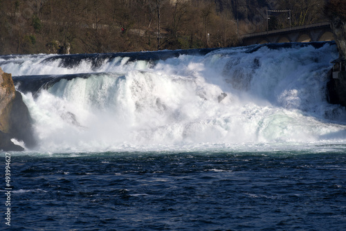 Famous Rhine Falls with rocks and splashing water on a sunny spring day, focus on background. Photo taken March 7th, 2022, Zurich, Switzerland.