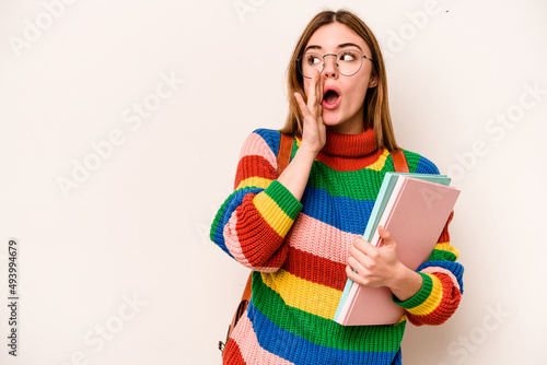 Young student caucasian woman isolated on white background is saying a secret hot braking news and looking aside