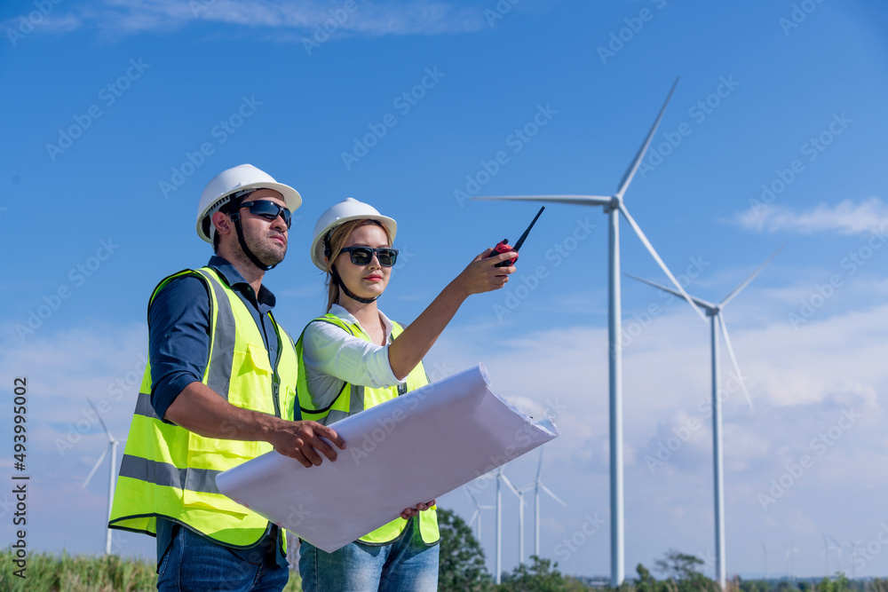 Engineer wearing uniform ,helmet hold document inspection work in wind turbine farms rotation to generate electricity energy. Green ecological power energy generation wind sustainable energy concept. Engineer wearing uniform ,helmet hold document inspection work in wind turbine farms rotation to generate electricity energy. Green ecological power energy generation wind sustainable energy concept.