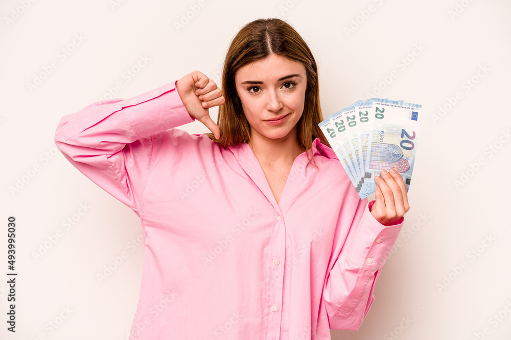 Young woman holding banknotes isolated on white background showing a dislike gesture, thumbs down. Disagreement concept. Young woman holding banknotes isolated on white background showing a dislike gesture, thumbs down. Disagreement concept.