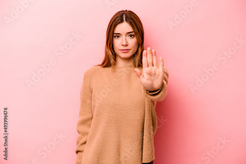 Young caucasian woman isolated on pink background standing with outstretched hand showing stop sign, preventing you. © Asier