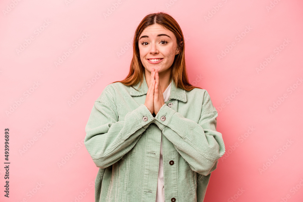 Young caucasian woman isolated on pink background holding hands in pray near mouth, feels confident. Young caucasian woman isolated on pink background holding hands in pray near mouth, feels confident.