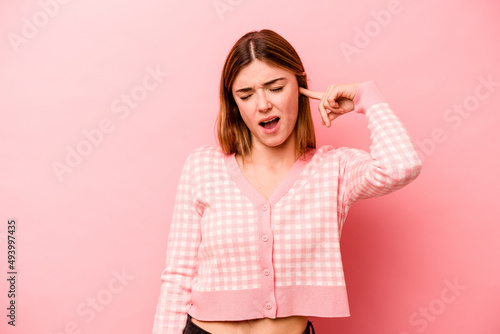 Young caucasian woman isolated on pink background covering ears with hands.