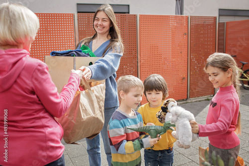 A senior woman gives Ukrainian family of refugee clothes and toys to support them because they had to flee Russian attack. Humanitarian aid and helping hand from world for Ukraine during the war