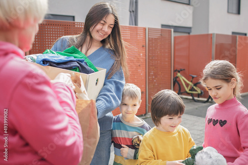 A senior woman gives Ukrainian family of refugee clothes and toys to support them because they had to flee Russian attack. Humanitarian aid and helping hand from world for Ukraine during the war