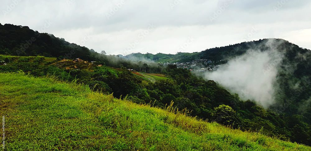 Obraz premium Beautiful range of green mountain, white cloud, small village and mist in the morning with copy space. Landscape view of hill at Phetchabun, Thailand. Natural wallpaper and Famous place for travel.