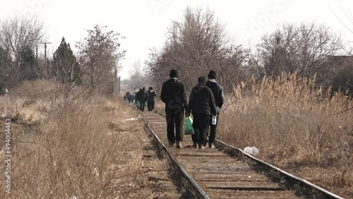 A telephoto video clip of dozens refugees walking on a train track in the distance, carrying all their belongings with them, in a cold, sunny winter day. some heat haze is apparent. photo