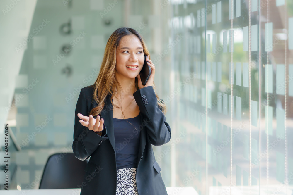 Pretty young Asian businesswoman standing talking on the phone in the office. Pretty young Asian businesswoman standing talking on the phone in the office.
