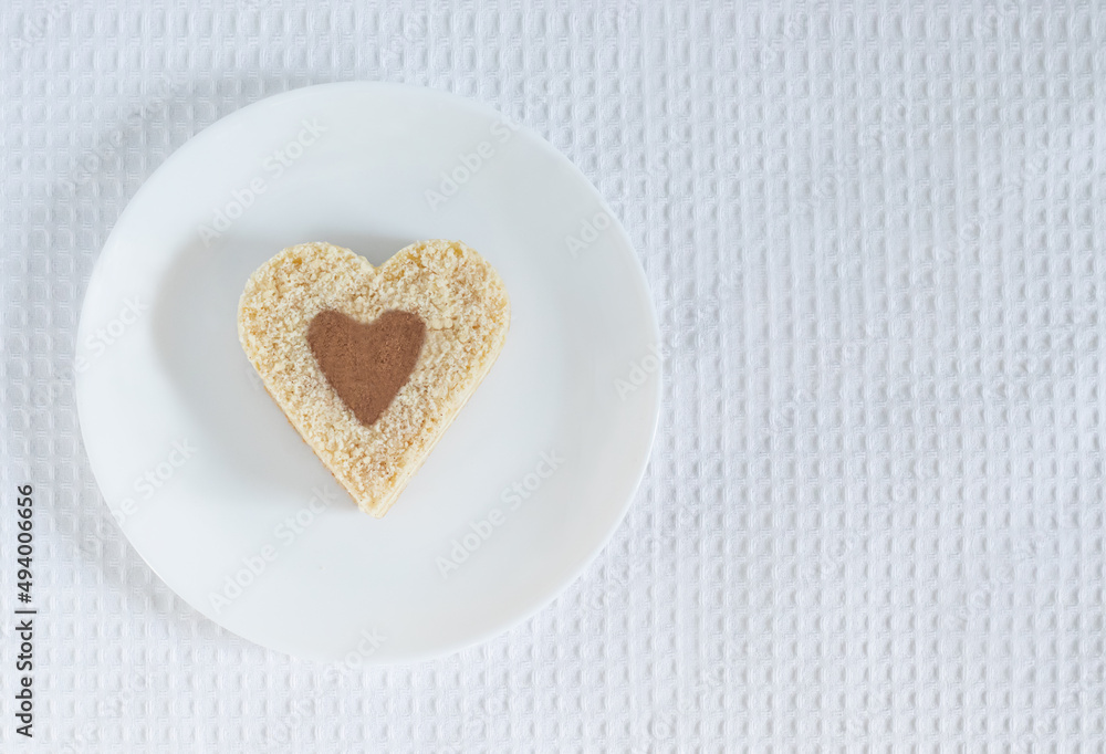 Top view of a heart-shaped cake sprinkled with cocoa lying on a white plate over a white tablecloth background Top view of a heart-shaped cake sprinkled with cocoa lying on a white plate over a white tablecloth background