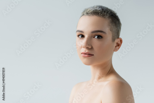 young woman with perfect skin, natural makeup and bare shoulders looking at camera isolated on grey.