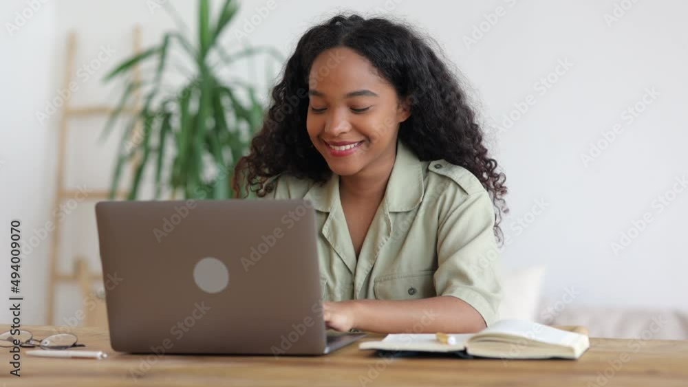 Young woman starting work with laptop and sitting at table in apartment room spbi. 4k Portrait of American African female opens network device and looks at screen with happy smile, types or surfs web Young woman starting work with laptop and sitting at table in apartment room spbi. 4k Portrait of American African female opens network device and looks at screen with happy smile, types or surfs web