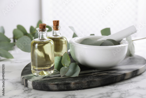Bottles of eucalyptus essential oil and plant branches on white marble table