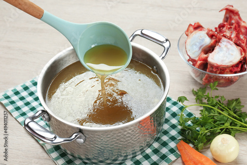 Delicious homemade bone broth and ingredients on wooden table photo