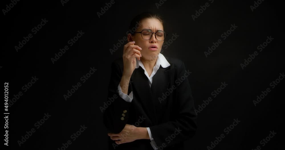 Businesswoman in glasses and office clothes experiences a coughing from vaping on isolated black background.Asian woman smokes an electronic cigarette.Nicotine addiction, harmful habit, health hazard. Businesswoman in glasses and office clothes experiences a coughing from vaping on isolated black background.Asian woman smokes an electronic cigarette.Nicotine addiction, harmful habit, health hazard.