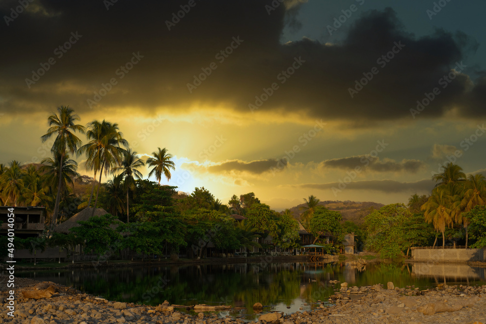 Obraz premium Sunset over touristic village in El Tunco, El Salvador with overcast. Huts covered by palm trees on the shore of Rio Grande river