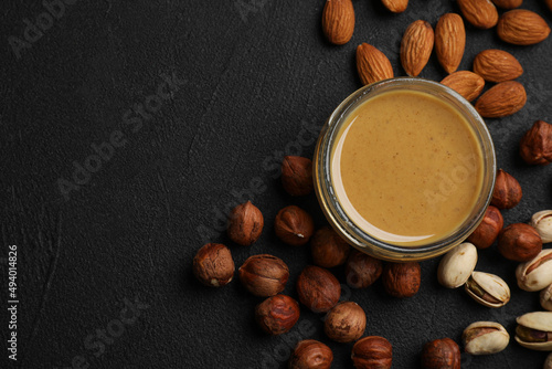 Delicious hazelnut butter and different nuts on black table, flat lay. Space for text