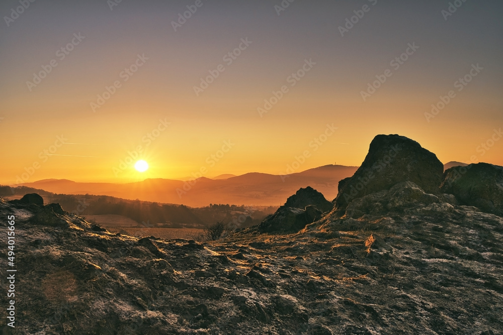 Sun peaking over the mountains in germany beside a large rock formation Sun peaking over the mountains in germany beside a large rock formation
