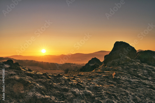 Sun peaking over the mountains in germany beside a large rock formation