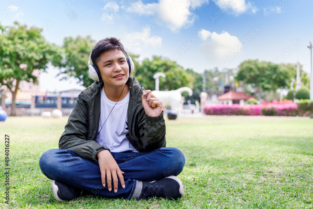 teenage student boy sitting on grren grass and listen to music with headphone relax in the lawn, park ,summer student concept,. teenage student boy sitting on grren grass and listen to music with headphone relax in the lawn, park ,summer student concept,.