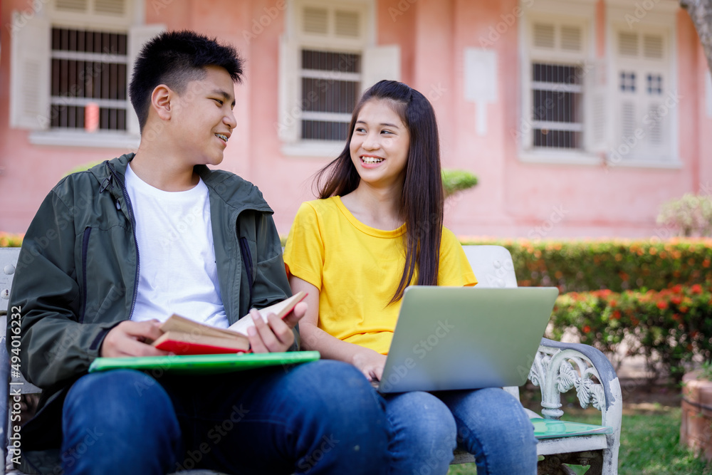 teenage student boy and girl sitting on chair reading book and working using laptop computer in the park ,summer student concept,. teenage student boy and girl sitting on chair reading book and working using laptop computer in the park ,summer student concept,.