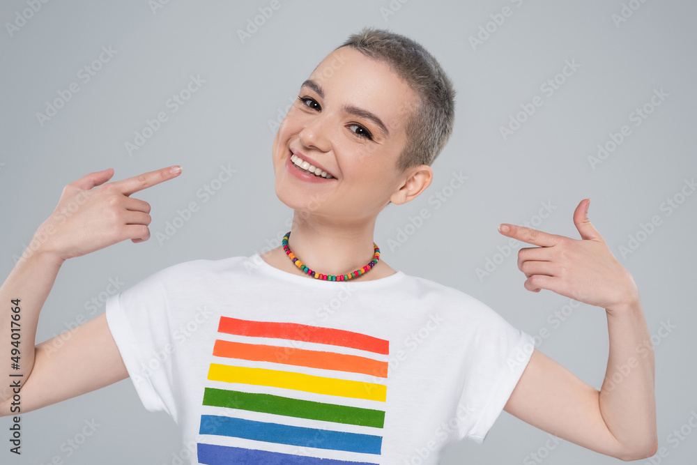 happy woman in rainbow colors t-shirt pointing with fingers at herself isolated on grey. happy woman in rainbow colors t-shirt pointing with fingers at herself isolated on grey.
