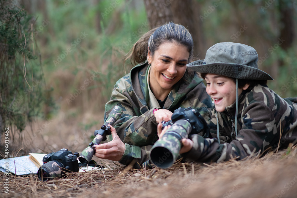 Interested family taking pictures in forest. Mother and son with modern cameras lying on ground, holding cameras, looking at pictures. Parenting, family, leisure concept