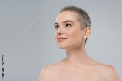 charming woman with naked shoulders smiling while looking away isolated on grey.