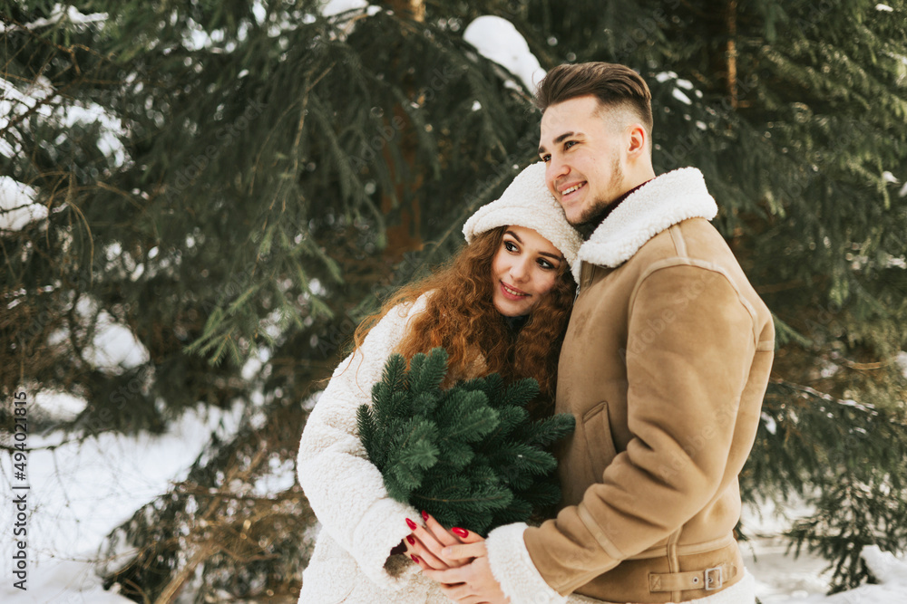 Obraz premium young couple in love man and woman in fashion stylish winter clothes standing in snowy pine forest and having fun spending time together, concept of valentine's day and newlyweds, tenderness and love
