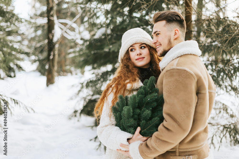 young couple in love man and woman in fashion stylish winter clothes standing in snowy pine forest and having fun spending time together, concept of valentine's day and newlyweds, tenderness and love