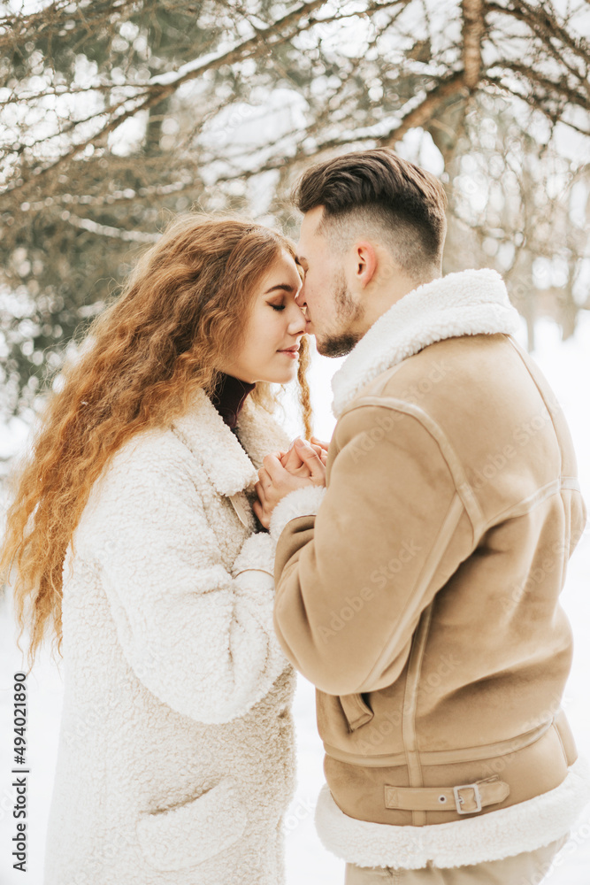 Fototapeta premium young couple in love man and woman in fashion stylish winter clothes standing in snowy pine forest and having fun spending time together, concept of valentine's day and newlyweds, tenderness and love