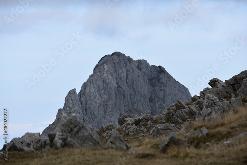 Scenic view of a rocky mountain peak seen behind a slope covered with dried grass and stones