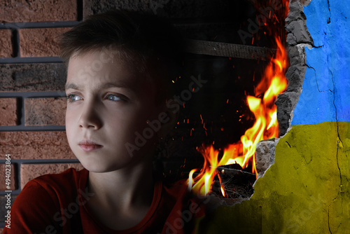 Sad little boy and wall of ruined building painted in color of national flag on fire. Stop war in Ukraine photo